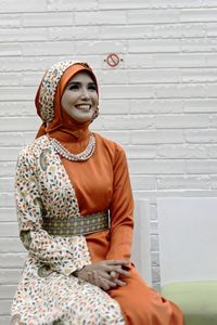 Smiling young woman sitting against white brick wall