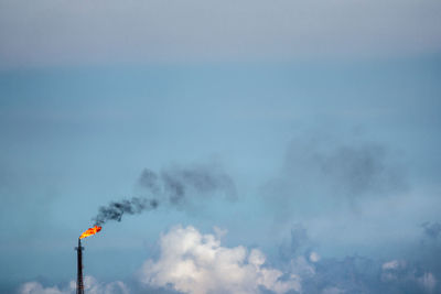 Fire emitting from smoke stack against cloudy sky