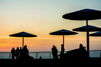 Silhouette people and parasols at beach against sky during sunset