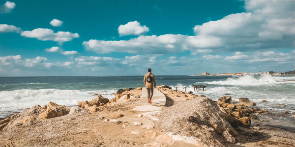 Man standing on rock at beach against sky