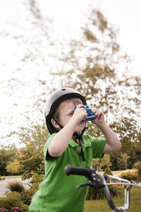 Boy photographing through camera while cycling at park