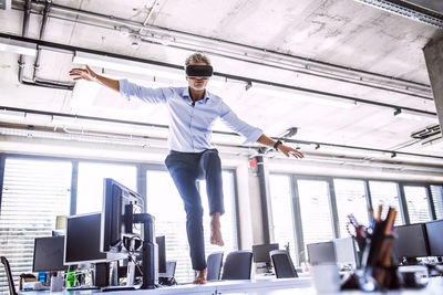 Barefoot mature businessman on desk in office wearing vr glasses barefoot