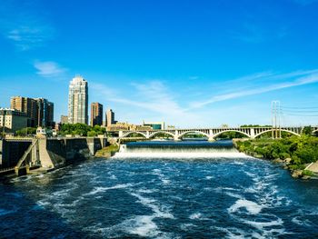 Bridge over river by buildings against blue sky