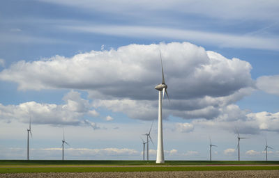 Wind turbines at field on sunny day under cloudy sky