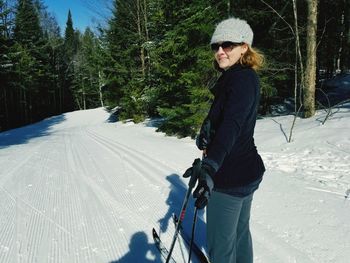 Portrait of smiling mature woman skiing on snow covered field in forest