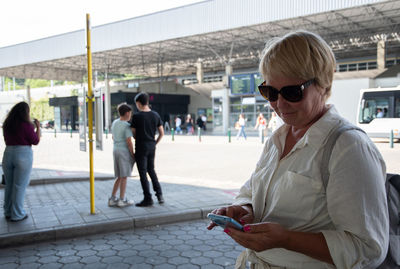 A middle-aged caucasian woman is waiting for a bus at a bus stop and writing