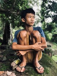 Young man looking away while sitting on tree