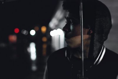 Close-up of boy looking away in illuminated city at night