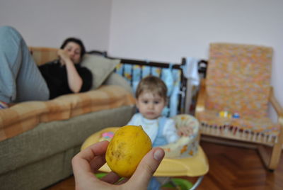 Cropped hand of woman giving lemon to son at home