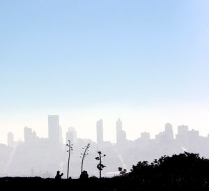 Silhouette trees and buildings against clear sky