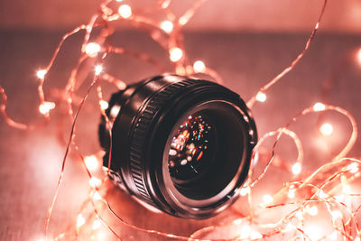 Close-up of camera lens surrounded by illuminated christmas lights at home