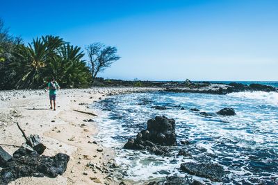 Rear view of young man with backpack walking at beach against clear blue sky