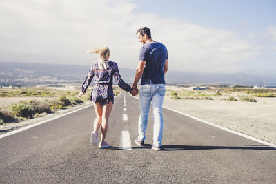 Rear view of couple holding hands while walking on road