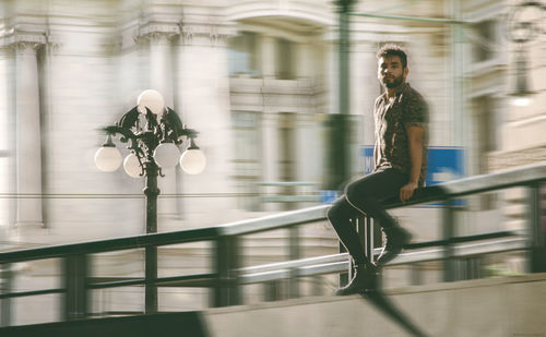 Blurred motion of man sitting on railing by road in city