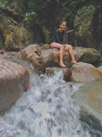 Portrait of woman sitting on rocks by waterfall