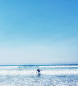 Woman surfing in sea against clear sky during sunny day