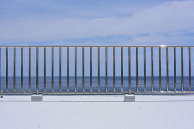 Metal railing by sea against sky