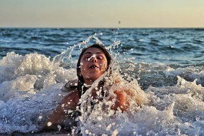 Portrait of young woman splashing water in sea