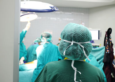 Rear view of surgeon looking at coworkers working in operating room