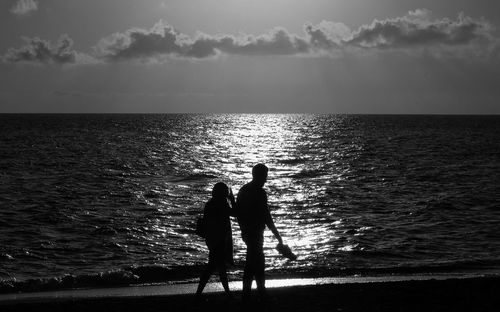 Silhouette people on beach against sky during sunset