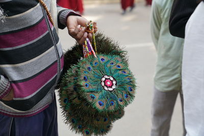 Midsection of man holding multi colored peafowl fans