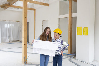Smiling sibling holding plan at construction site