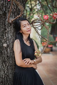 Portrait of young woman standing against tree trunk