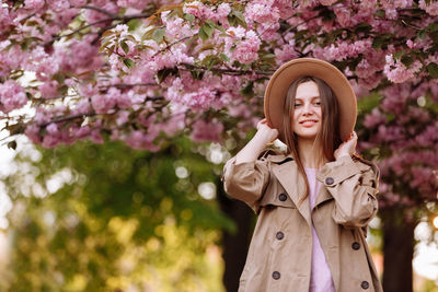 Portrait of smiling young woman standing by pink flower