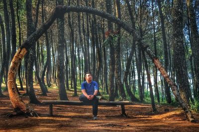 Full length of man sitting on log against trees at forest