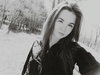 Portrait of beautiful young woman standing against trees