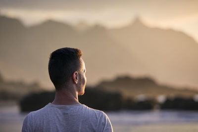 Portrait of pensive man on beach aganinst cliff at golden sunset. tenerife, canary islands, spain.