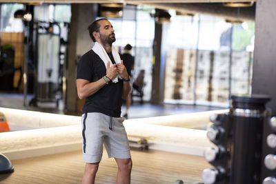 Exhausted bearded male athlete with towel closing eyes and resting after fitness workout in modern gym