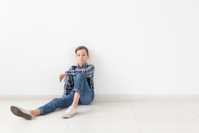 Portrait of young woman sitting against wall