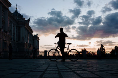 Silhouette man riding bicycle on street against sky