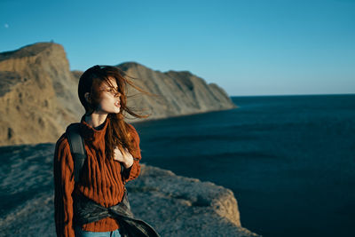 Man standing on rock by sea against clear sky