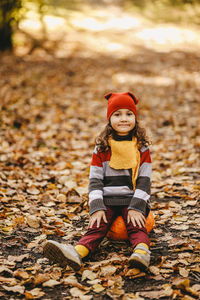 Happy cute little girl child in warm bright clothes sitting on a pumpkin in the autumn park outdoors
