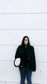 Portrait of young woman standing against wall