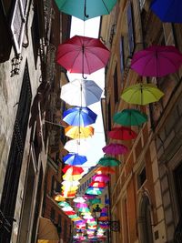 Low angle view of multi colored umbrellas hanging amidst buildings in city