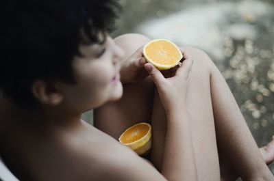 Close-up of shirtless boy eating orange