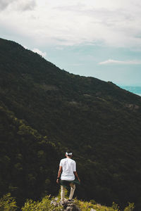 Rear view of man standing on mountain against sky