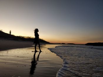 Silhouette young woman standing at beach against clear sky