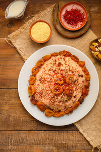 Couscous masfouf with almond milk in a plate on a wooden table next to saffron, nuts and couscous