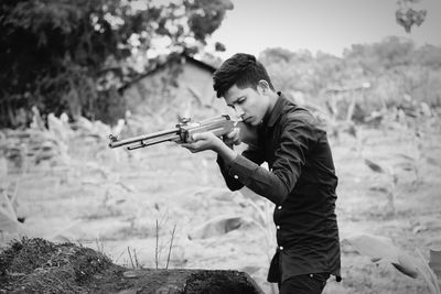 Young man aiming with rifle while standing at farm
