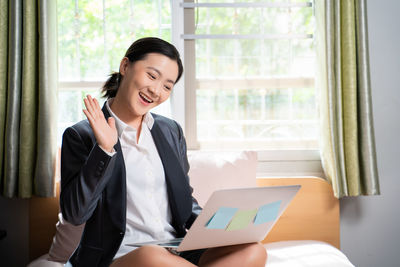 Young woman using phone while standing on window