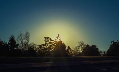 Silhouette trees by road against sky at sunset