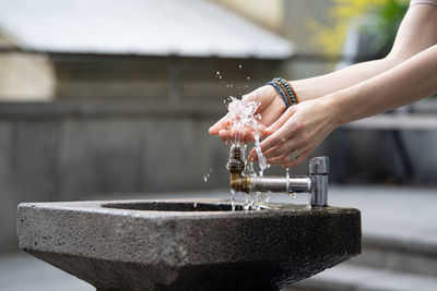 Hands with water pouring from tap in street. drops of water streaming up on fingers of young girl.