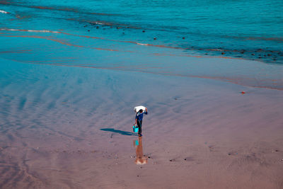 High angle view of man carrying sack on shoulders while walking on shore of beach