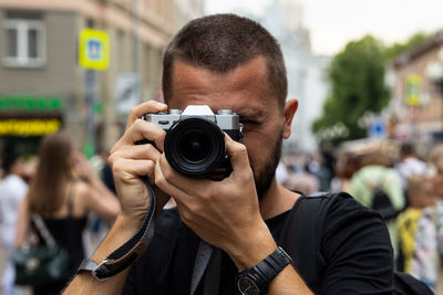 Portrait of caucasian photographer taking a picture with a retro style camera at crowded city
