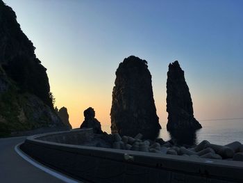 Rock formation by sea against clear sky