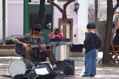 Street musician playing guitar on footpath in city